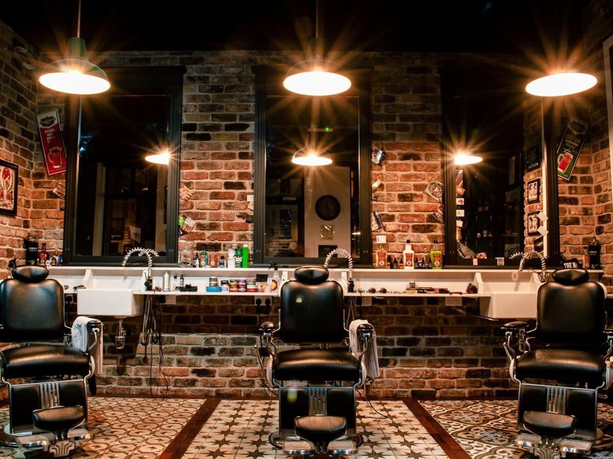 A barbershop with leather barber chairs, warm lights and brick walls