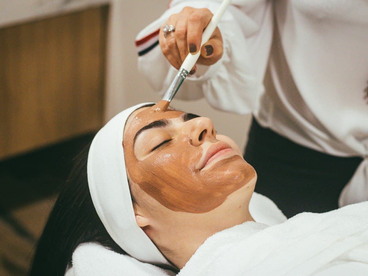 A beautician applying a face mask with a brush during a facial